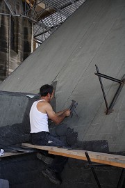 Ein Dachdecker schlägt mit einem Hammer und einer Haubrücke einen Schieferstein zu